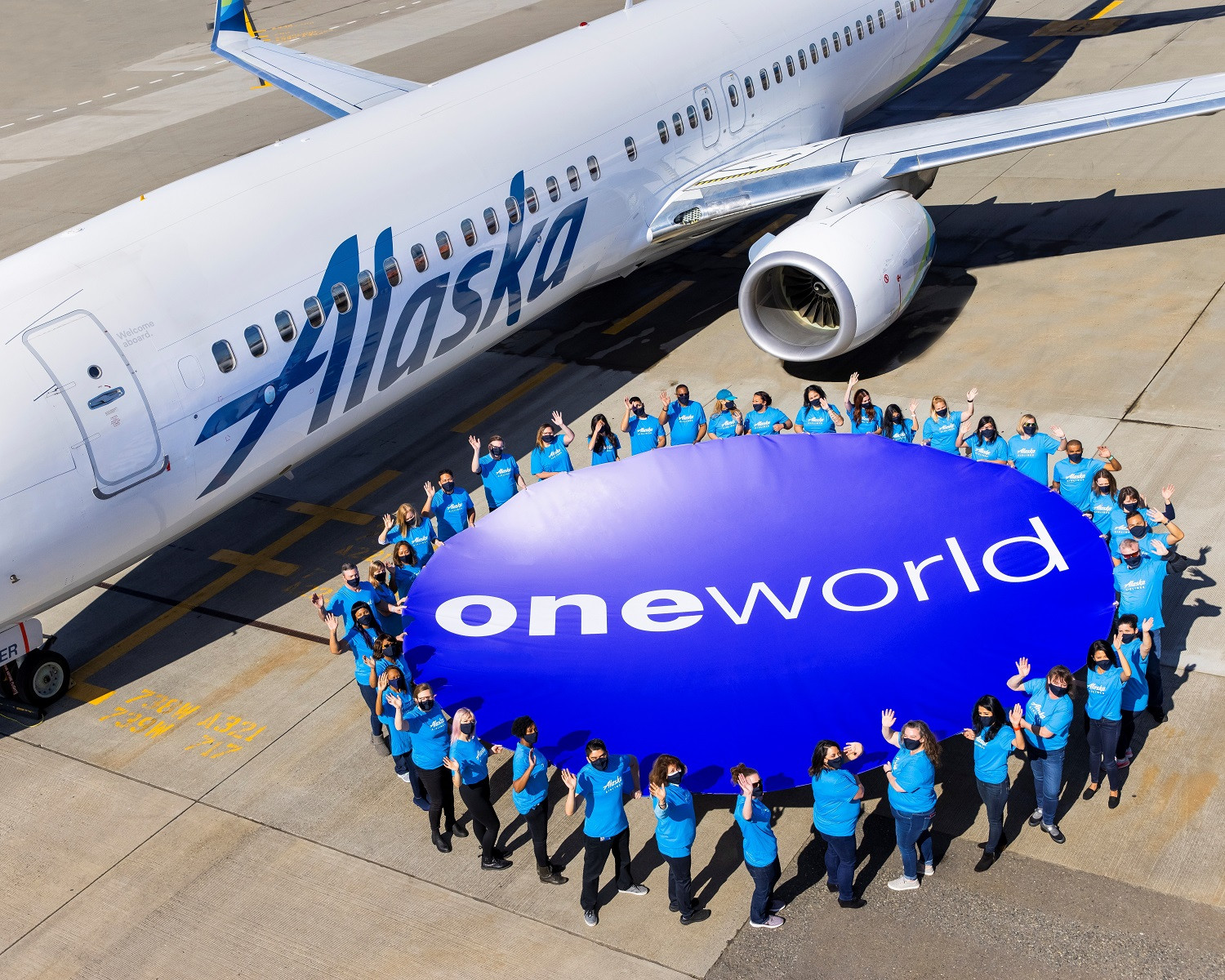 people hold a large Oneworld sign next to an Alaska Airlines plane