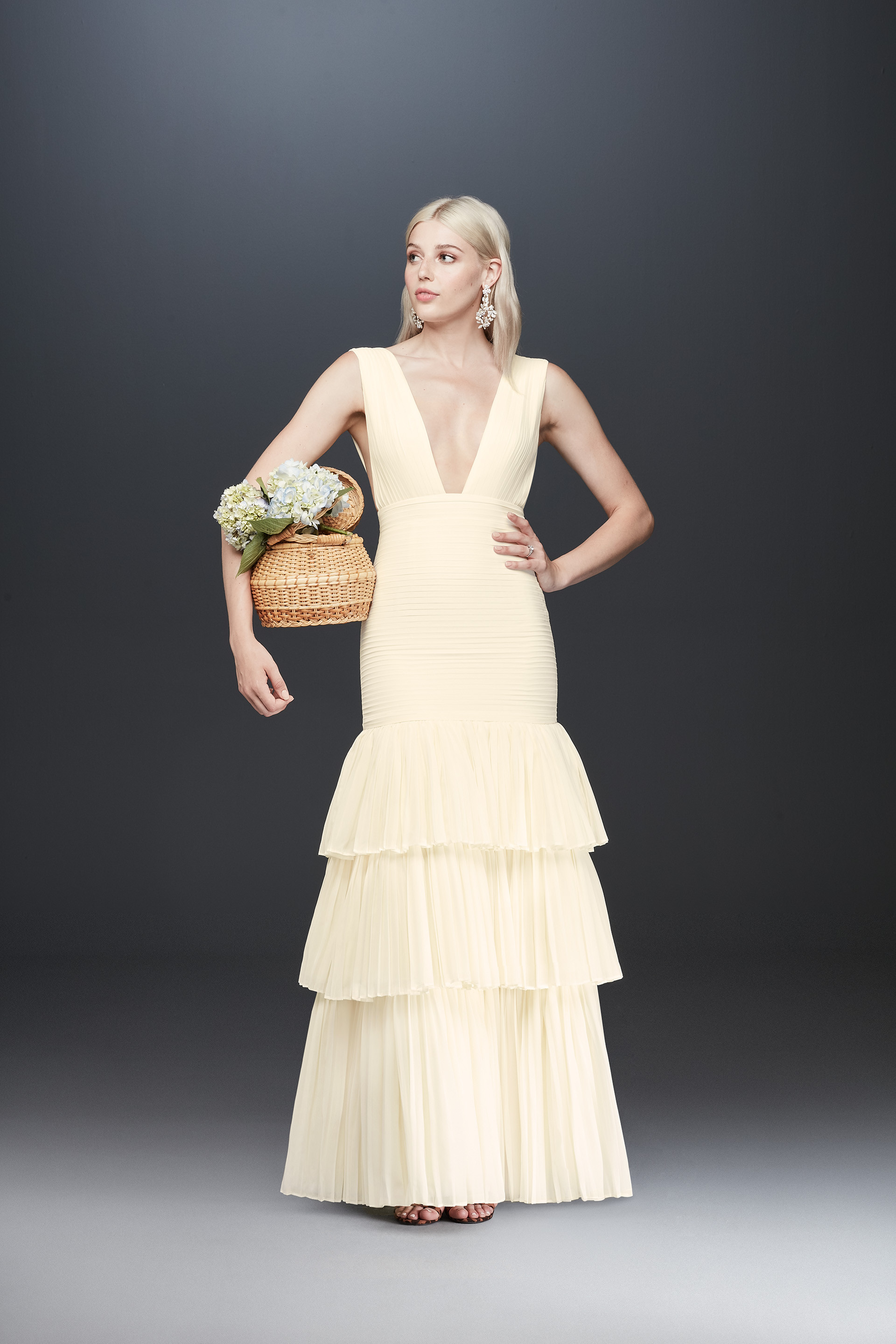 Bride holding woven basket in tiered long dress with plunging neckline, Fame and Partners x David's Bridal collaboration