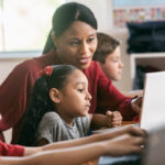 A classroom with students and a teacher assisting them.