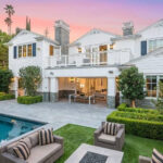 Luxury home with a lush green lawn and a "For Sale" sign indicating a high-value property, downpayment required