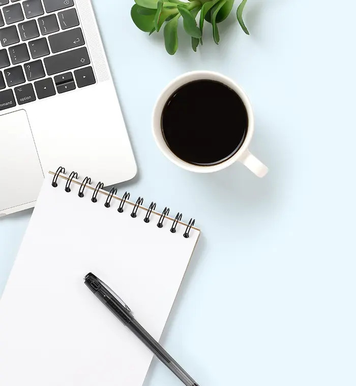 An open notebook with financial data, surrounded by a calculator, pen, and coffee mug