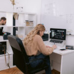 A female trader sits at a desk with a laptop and analyzes stock data.