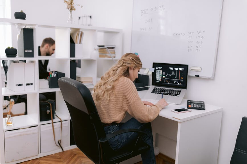A female trader sits at a desk with a laptop and analyzes stock data.