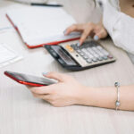 Young woman using a calculator and smartphone while analyzing finances