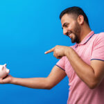 Excited Hispanic Man Holding Piggy Bank, signifying financial stability needed for car loans