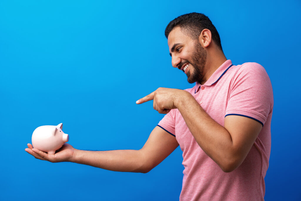 Excited Hispanic Man Holding Piggy Bank, signifying financial stability needed for car loans