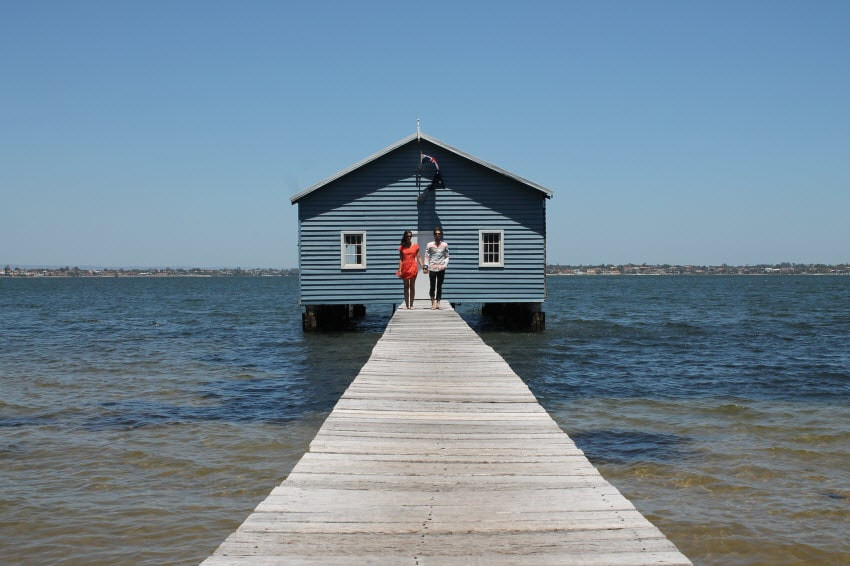 Fun Fact House on the water with a long dock and a couple holding hands in the distance.