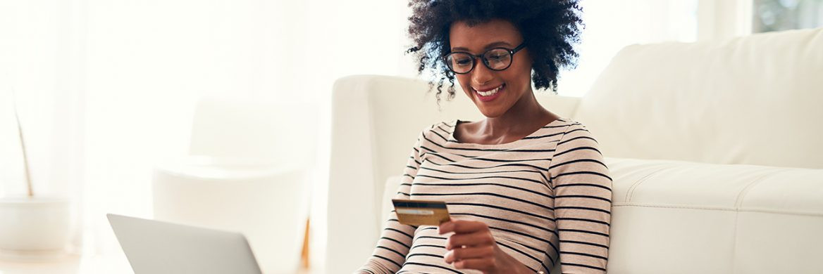 A woman smiles while looking at a debit card with her laptop open.