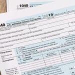 A person is reviewing a 1040 tax return document with a calculator on a desk.