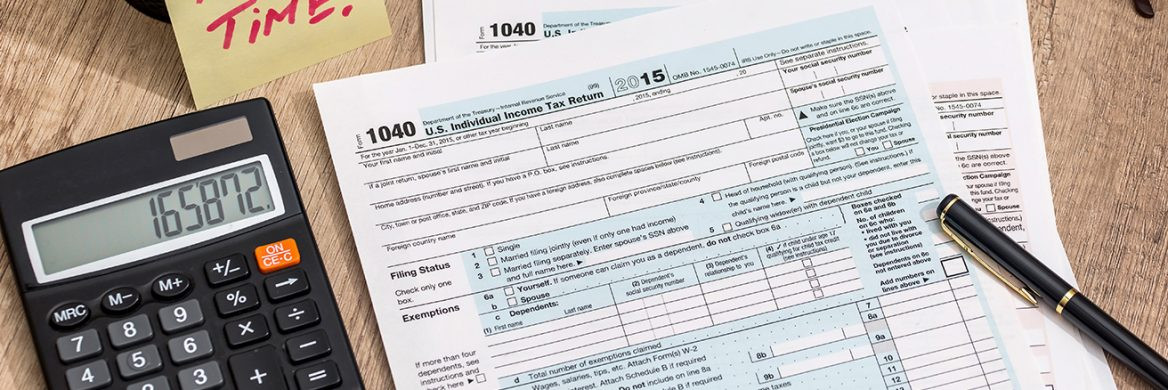 A person is reviewing a 1040 tax return document with a calculator on a desk.