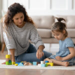 A young babysitter playing with a child with building blocks, illustrating the earnings that need to be reported for tax purposes.
