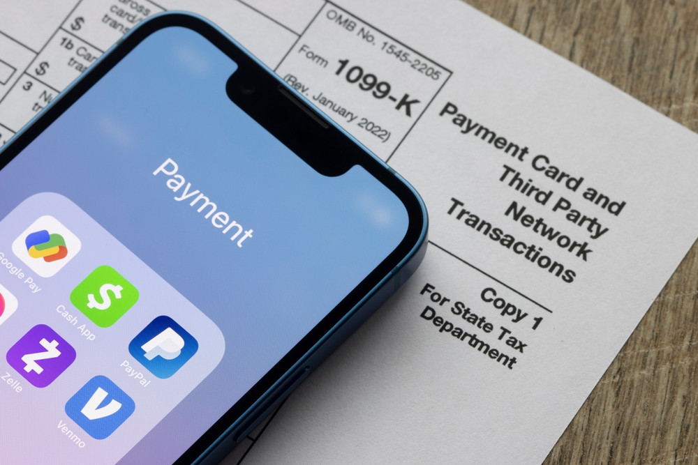 Payment apps like PayPal and Venmo are seen on an iPhone on top of Form 1099-k, displaying the modern methods of income reporting through third-party processors.