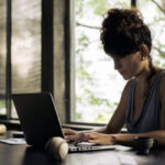 Person calculating taxes with a calculator, tax form, and laptop