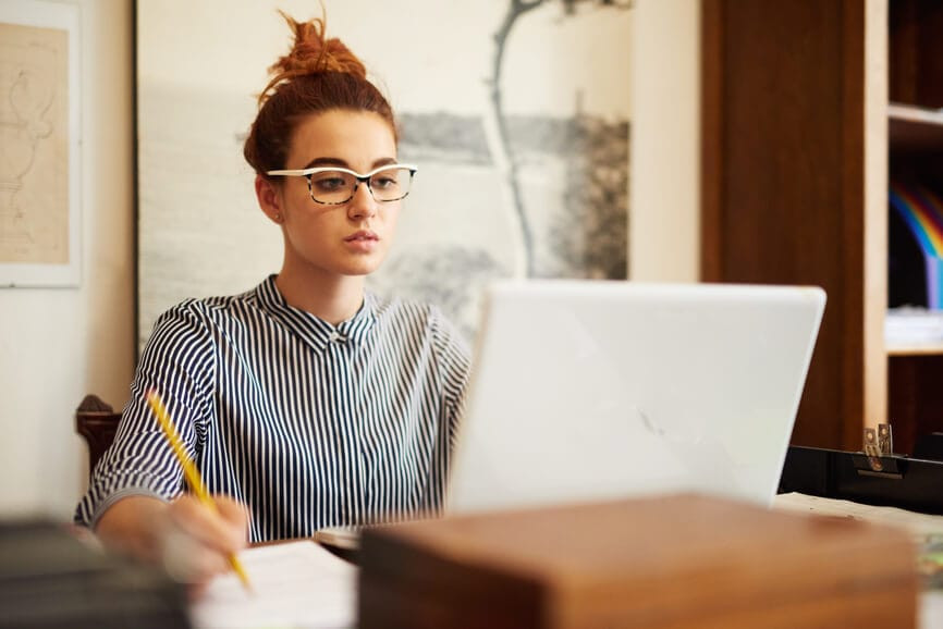 Young woman using computer and writing