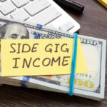 A stack of money and an inscription Side gig income on it, symbolizing extra income through a side job