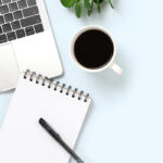 Laptop, notebook, pen, coffee, and plant on a table
