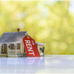 A toy house and a calculator on a table, symbolizing the calculation of rental income and its potential effect on SSI benefits.